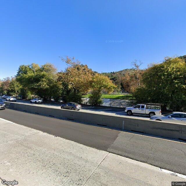 Street view along S Avenue 49 near HCM-482, showing the mature oaks and 110-freeway-adjacent setting that conceal the mansion from public street view.
