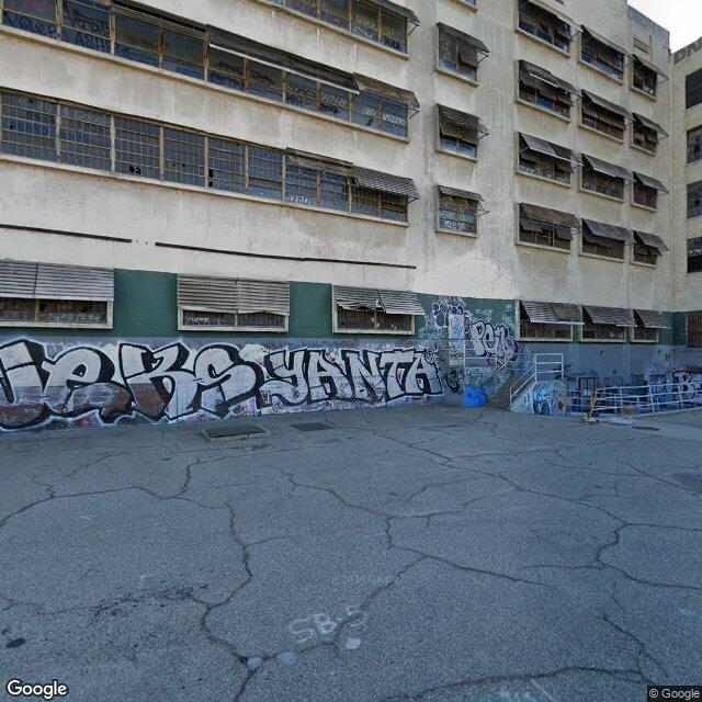 Existing-conditions street view of HCM-587 Lincoln Heights Jail showing graffiti-covered facade, boarded windows, perimeter cracked asphalt — long-term abandonment.